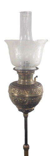 Close-up of an Antique Bradley & Hubbard Piano Oil Lamp from 1888. The lamp features a brass base with intricate detailing, a slender stem, and a glass shade with etched patterns. The lamp exudes elegance and vintage charm, showcasing the craftsmanship of the Victorian era